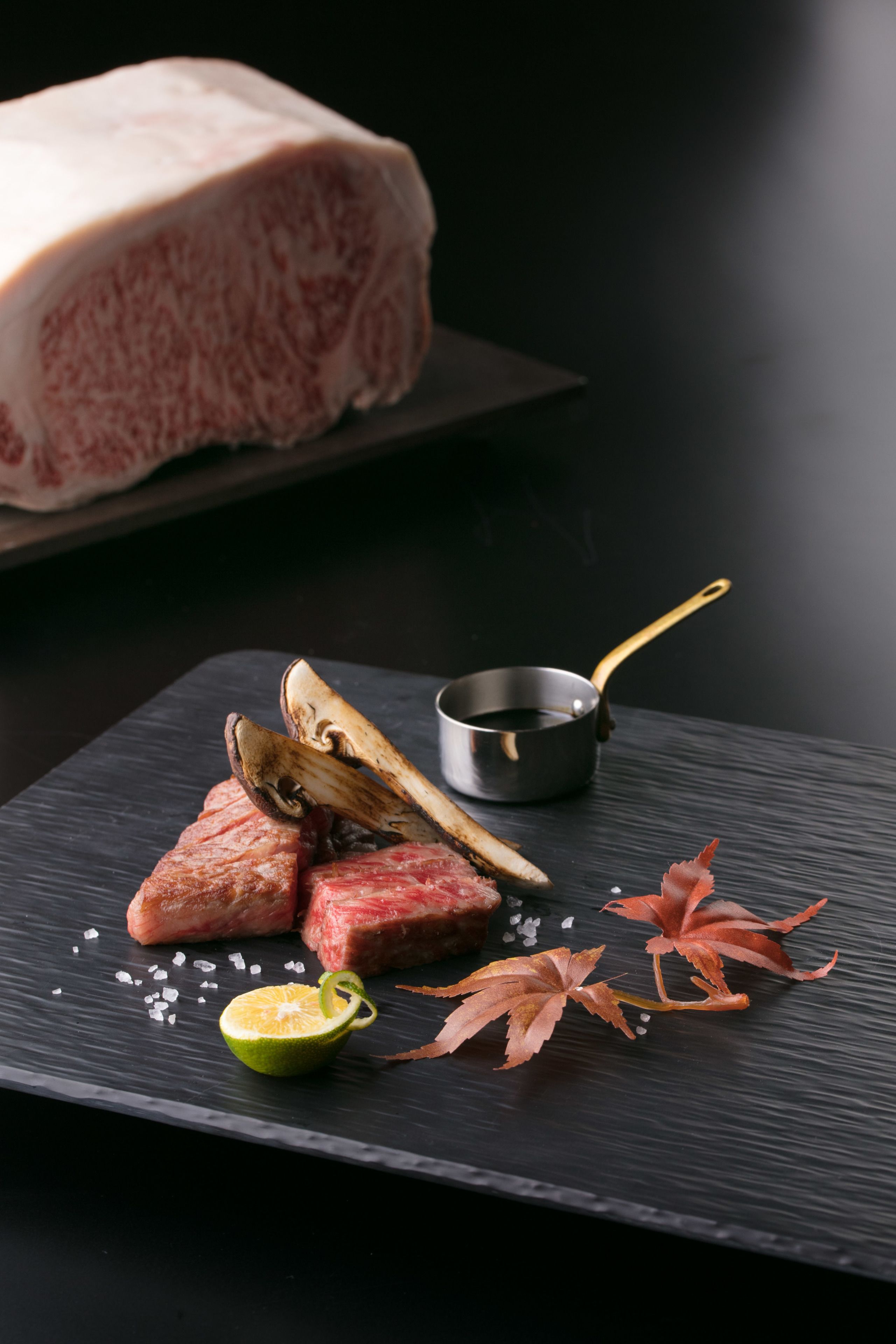 Un tagliere in ardesia nera con un pezzo di carne, mezzo lime e alcune foglie.