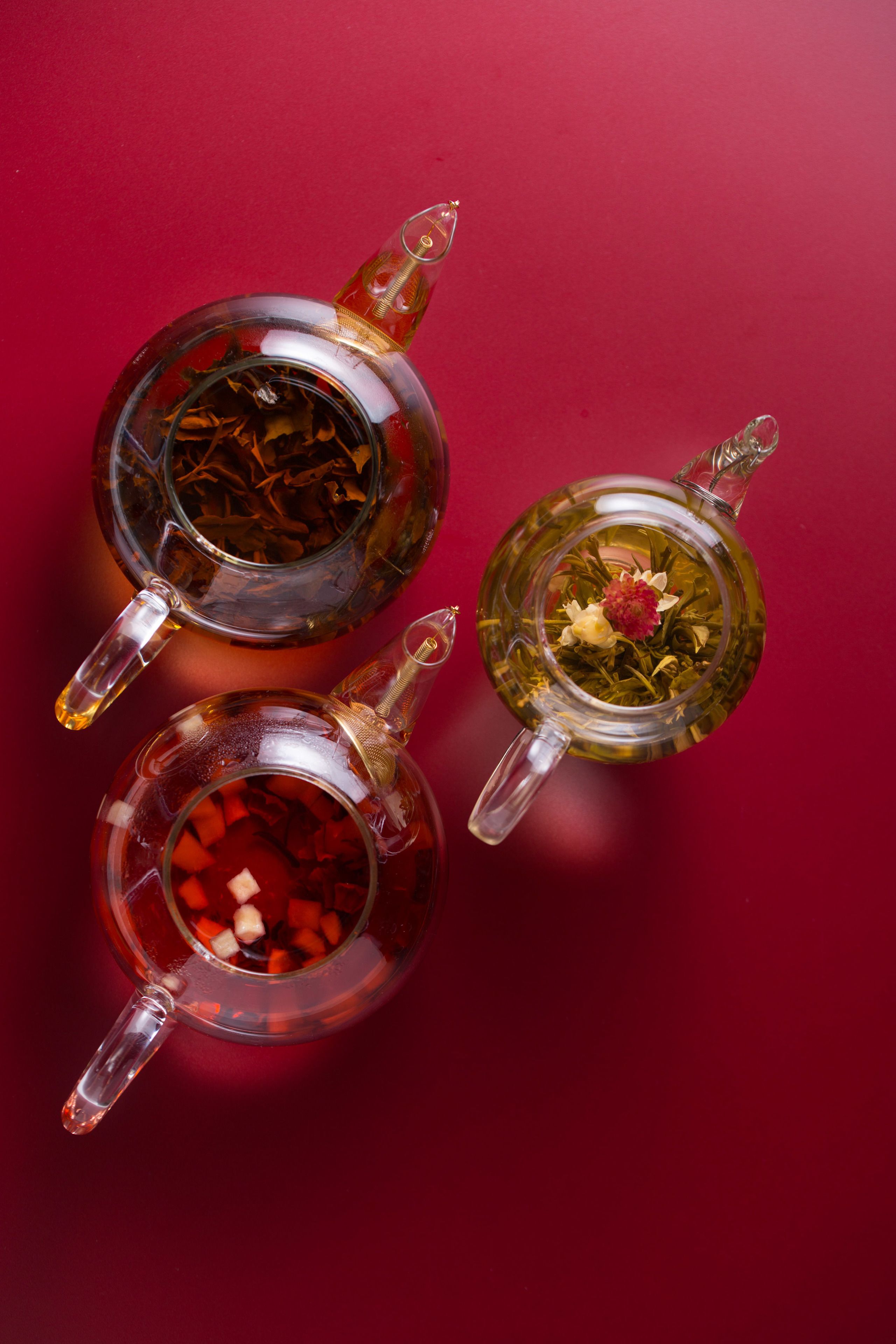 Three glass teapots with different contents on a red background.