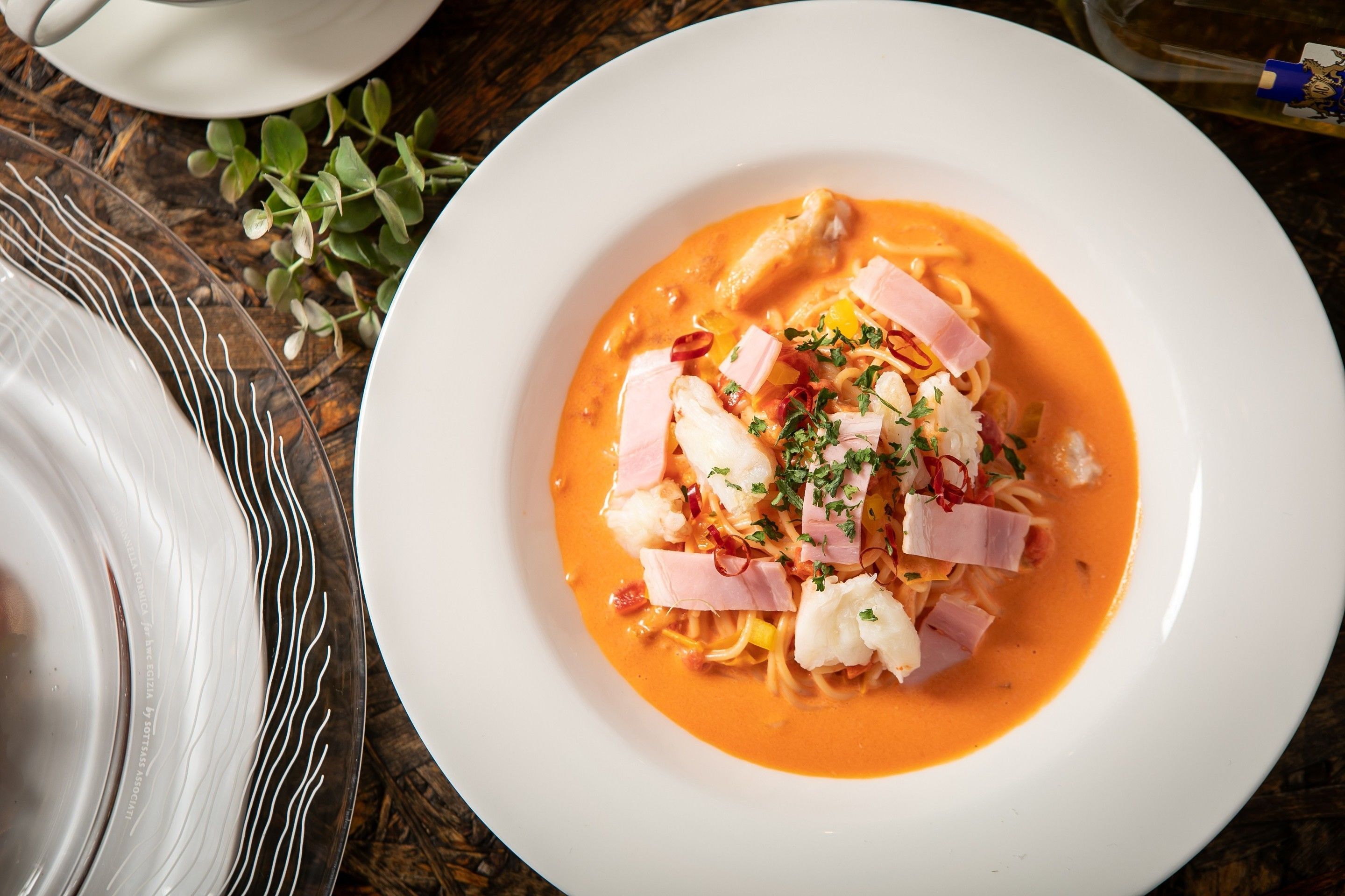 A white plate with pasta and seafood on a wooden table.