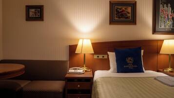 Une chambre d’hôtel avec un lit, deux lampes de chevet, une table de chevet avec un téléphone, un oreiller bleu orné d’un logo, un canapé et une petite table.