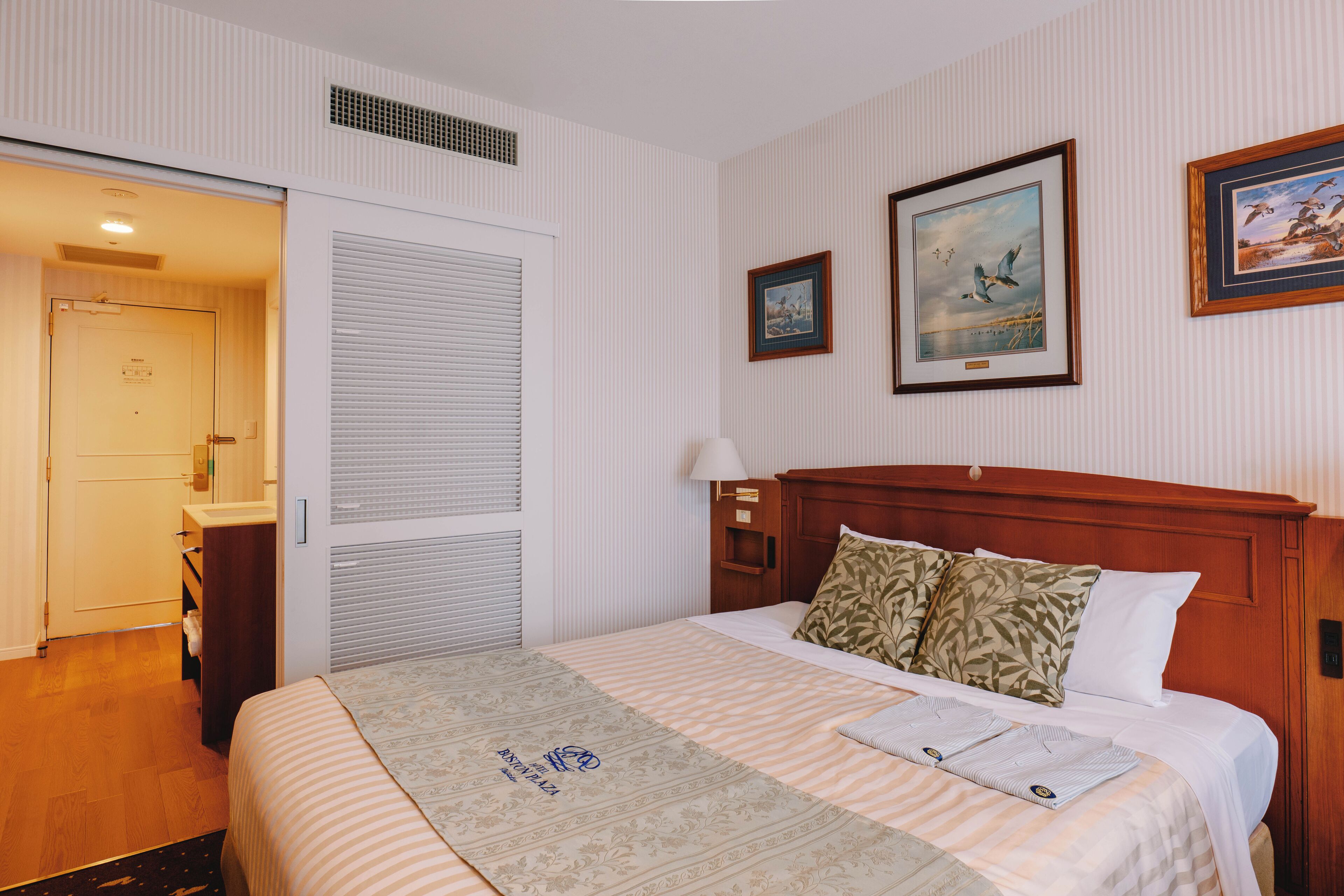 A hotel room with a bed, a nightstand, a lamp, and two framed pictures on the wall.