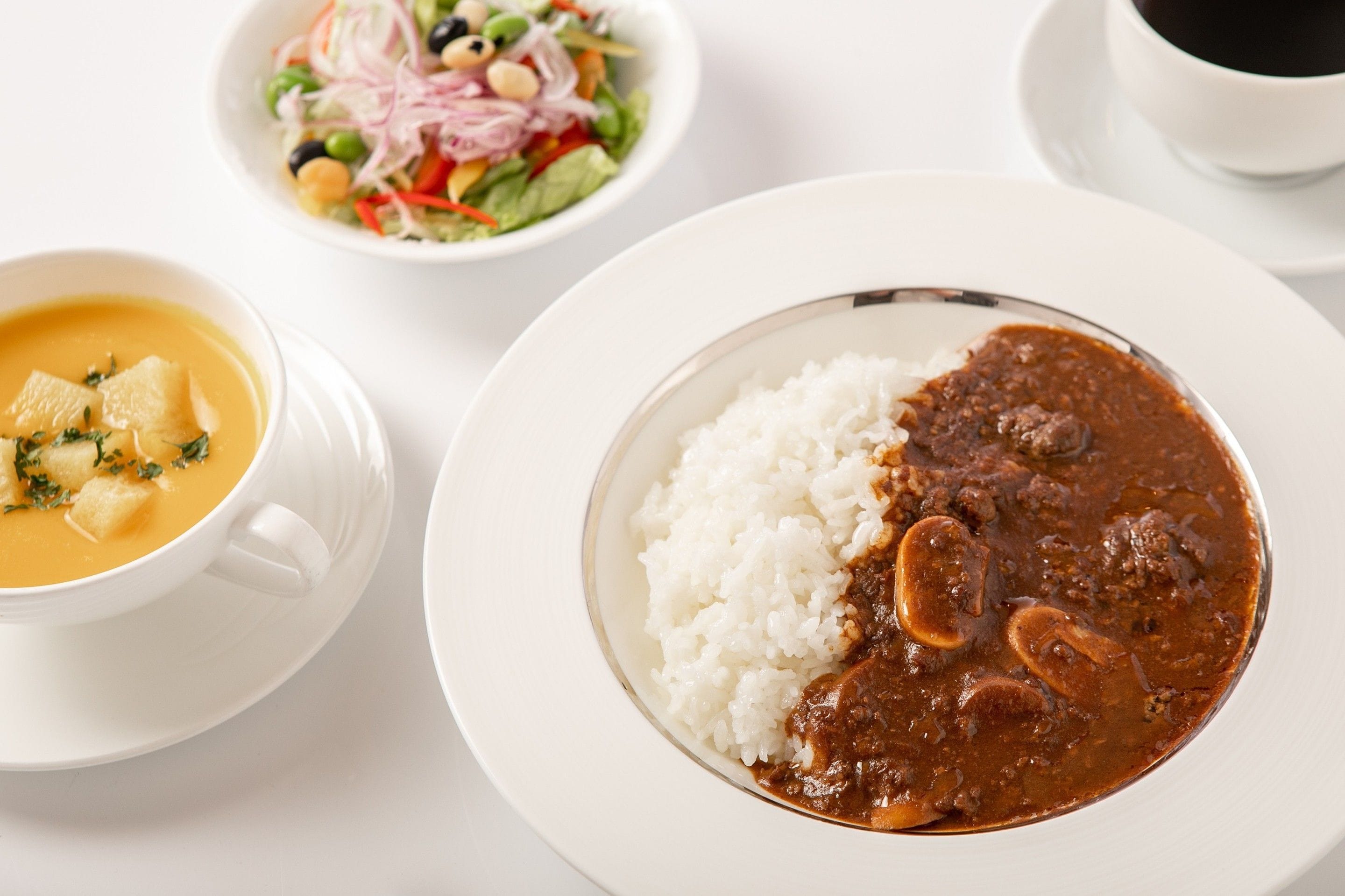 Un plato de arroz blanco con salsa marrón y champiñones, un tazón de sopa con trozos y una ensalada con diversas verduras.