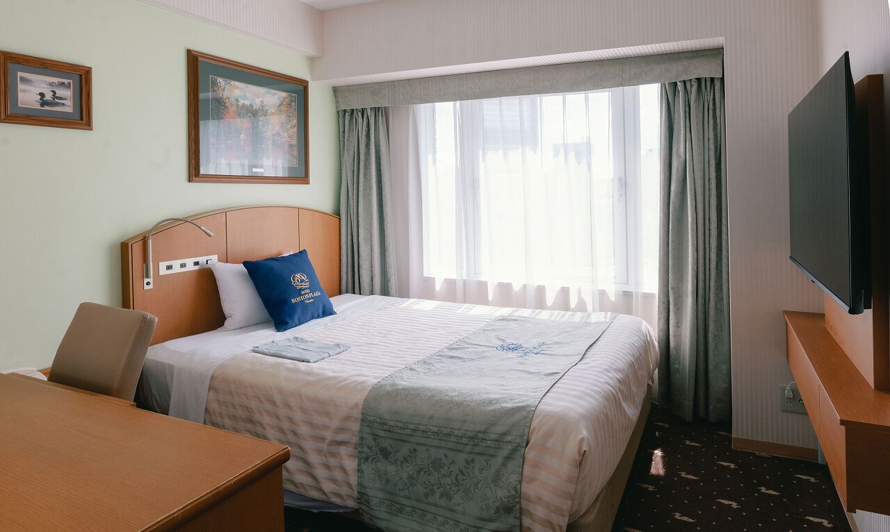 A hotel room with a bed, a desk, a chair, a TV, and a window with curtains.