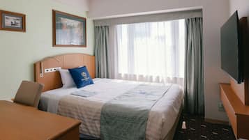 A hotel room with a bed, a desk, a chair, a TV, and a window with curtains.