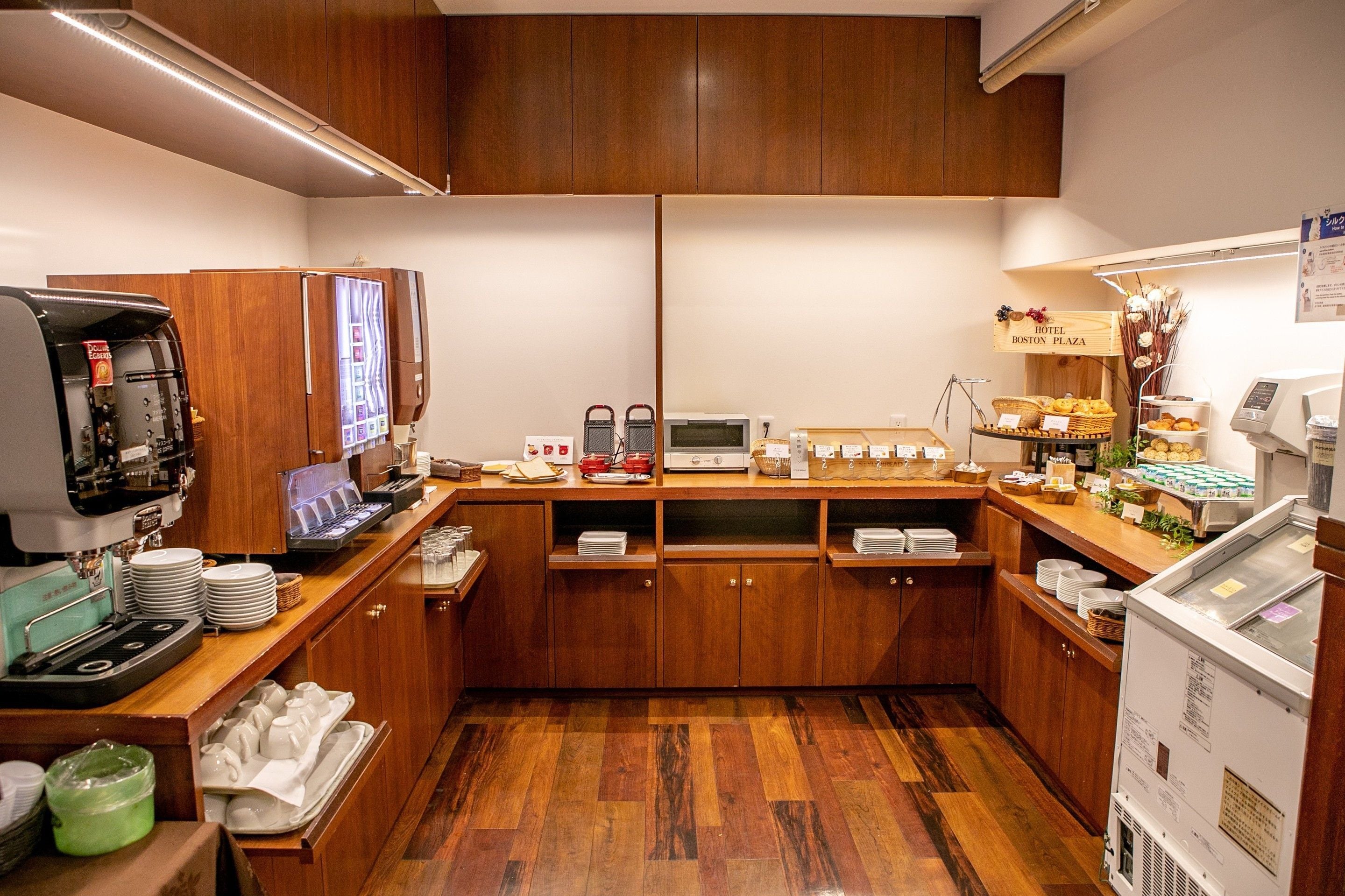A hotel kitchen with wooden cabinets, a coffee machine, a refrigerator, and a display case with pastries.