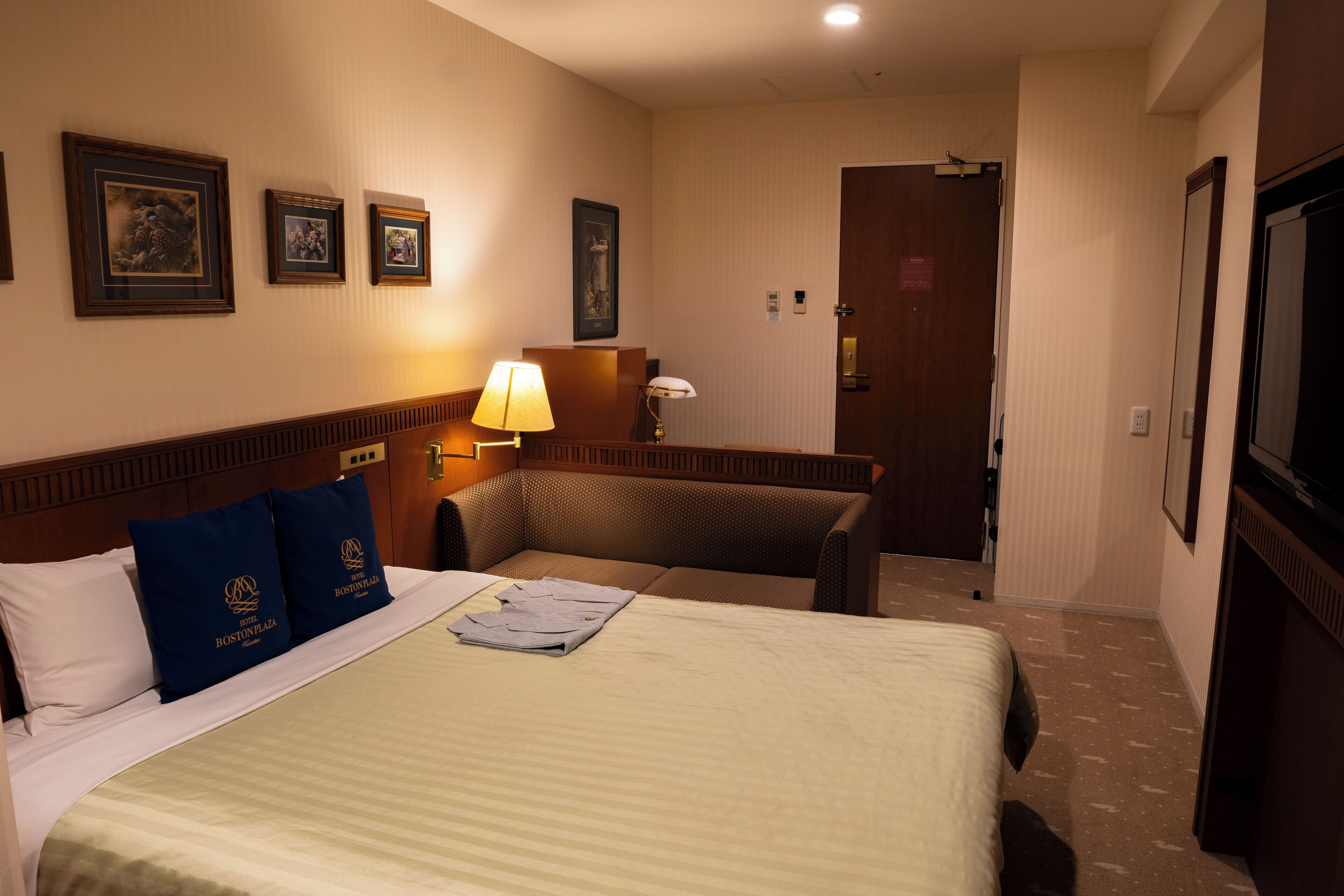 A hotel room with a large bed, two pillows, a desk, a chair, and a lamp.