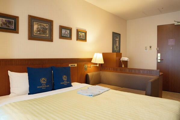 Habitación de hotel con una cama grande, dos almohadas, una mesita de noche, una lámpara y una puerta.
