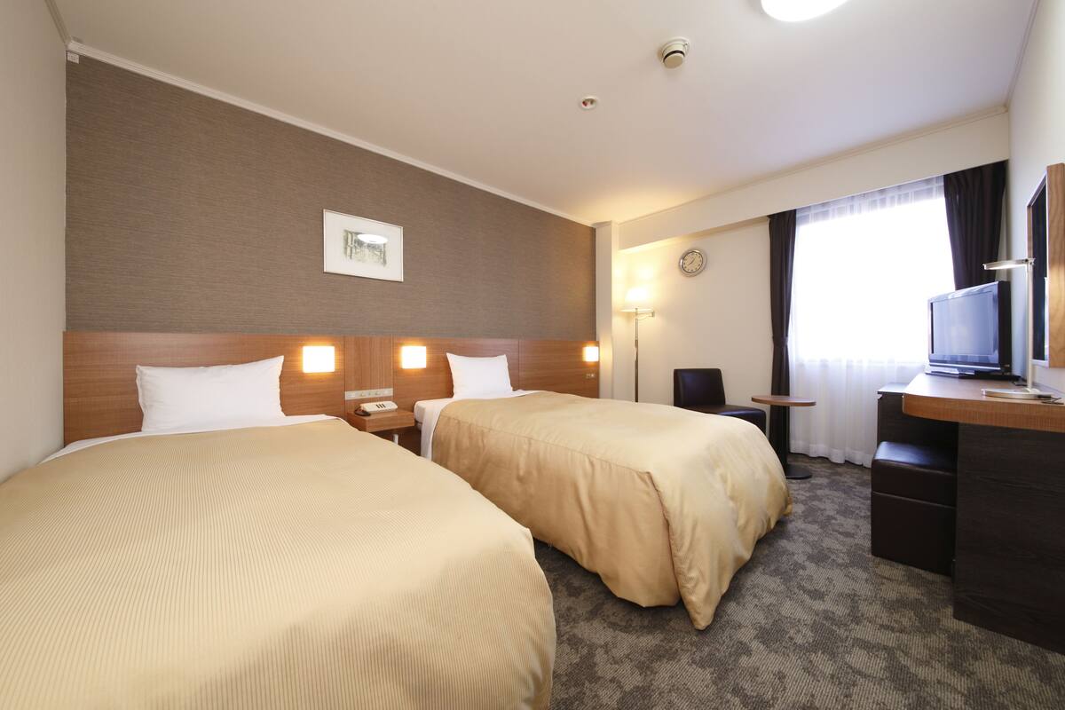 A hotel room with two beds, a desk, a TV, and a lamp.