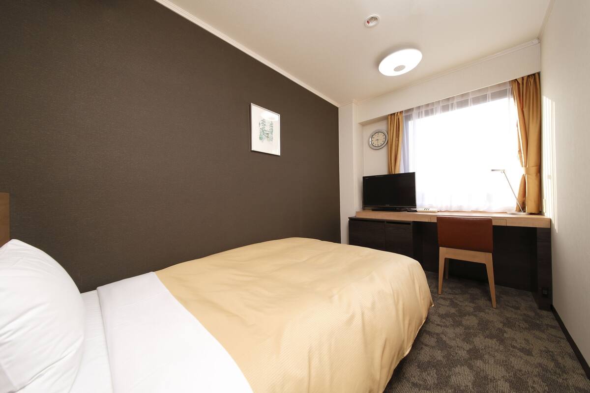 A hotel room with a bed, a desk, a chair, a television, and a window with curtains.