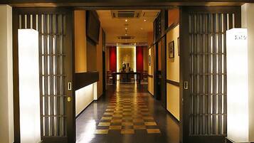 A hotel corridor with a checkered floor, a reception desk, and a dining area in the distance.