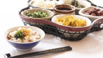 A variety of dishes in bowls and a basket, including rice, noodles, and dumplings, with chopsticks placed in front.