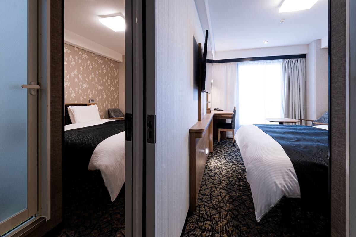 Habitación de hotel con dos camas, un escritorio, un televisor y una ventana con cortinas.