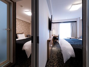 Habitación de hotel con dos camas, un escritorio, un televisor y una ventana con cortinas.