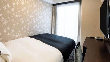 A hotel room with a bed, a desk, a chair, a television, and a window with curtains.