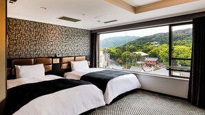 Ein Hotelzimmer mit zwei Betten, einer Wand mit Muster und einem großen Fenster mit Blick auf ein traditionelles Gebäude und Hügel.