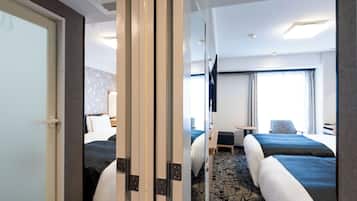 A hotel room with two beds, a desk, a chair, and a TV.