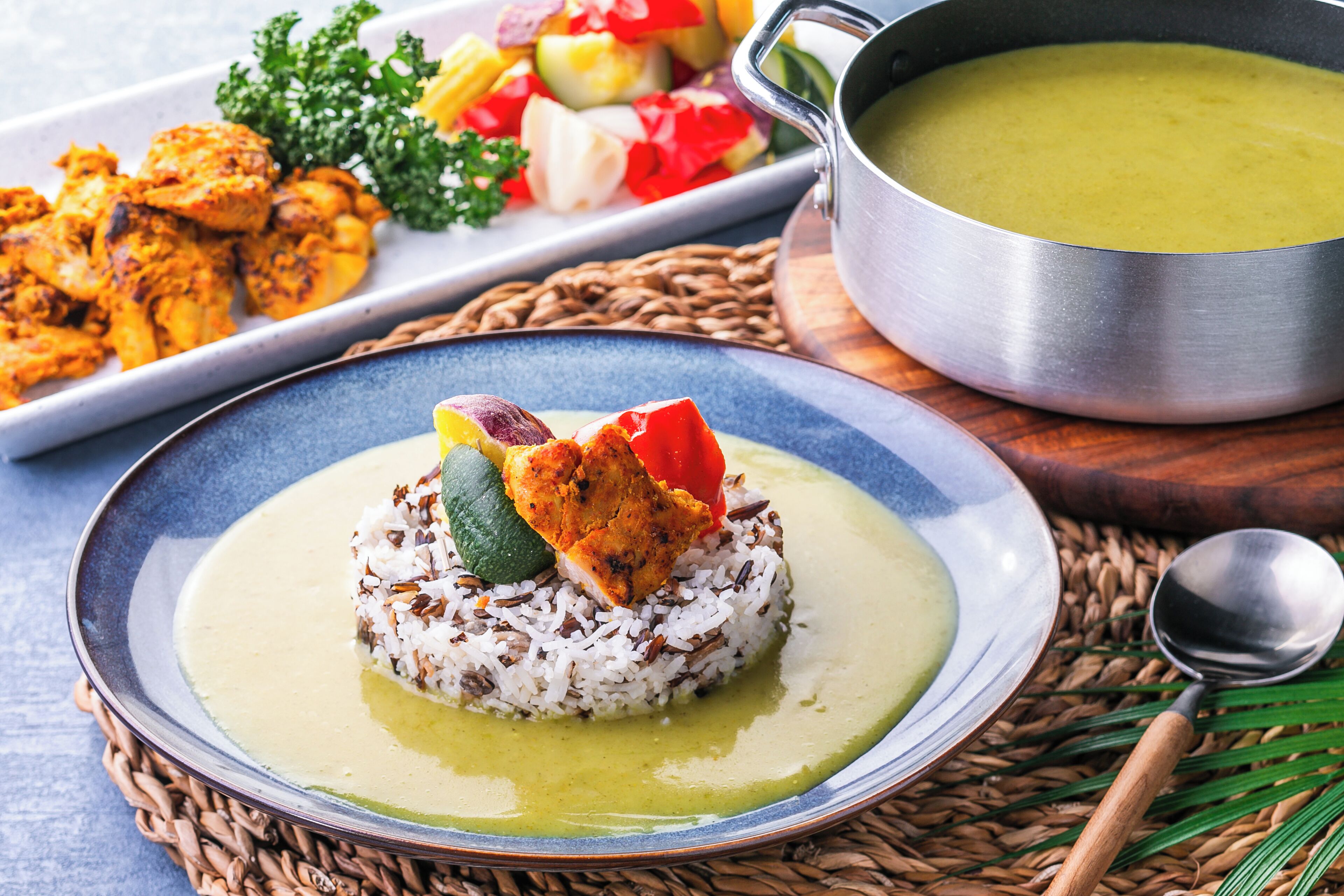 A plate of rice with vegetables and a piece of chicken, a bowl of soup, and a plate of grilled chicken and vegetables.