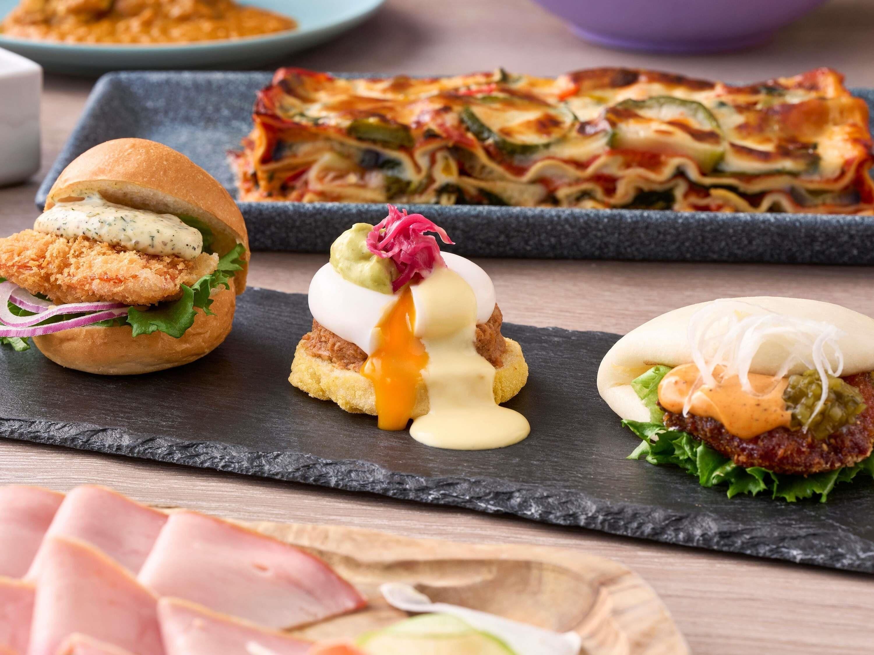 A variety of dishes including a sandwich, a pasta dish, and a burger, all served on a slate board.