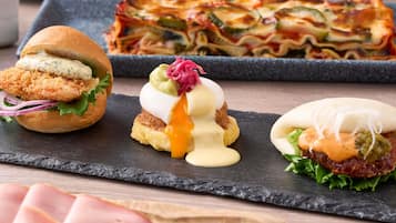 Variedad de platos, incluyendo un sándwich, pasta y una hamburguesa, todo servido sobre una tabla de pizarra.