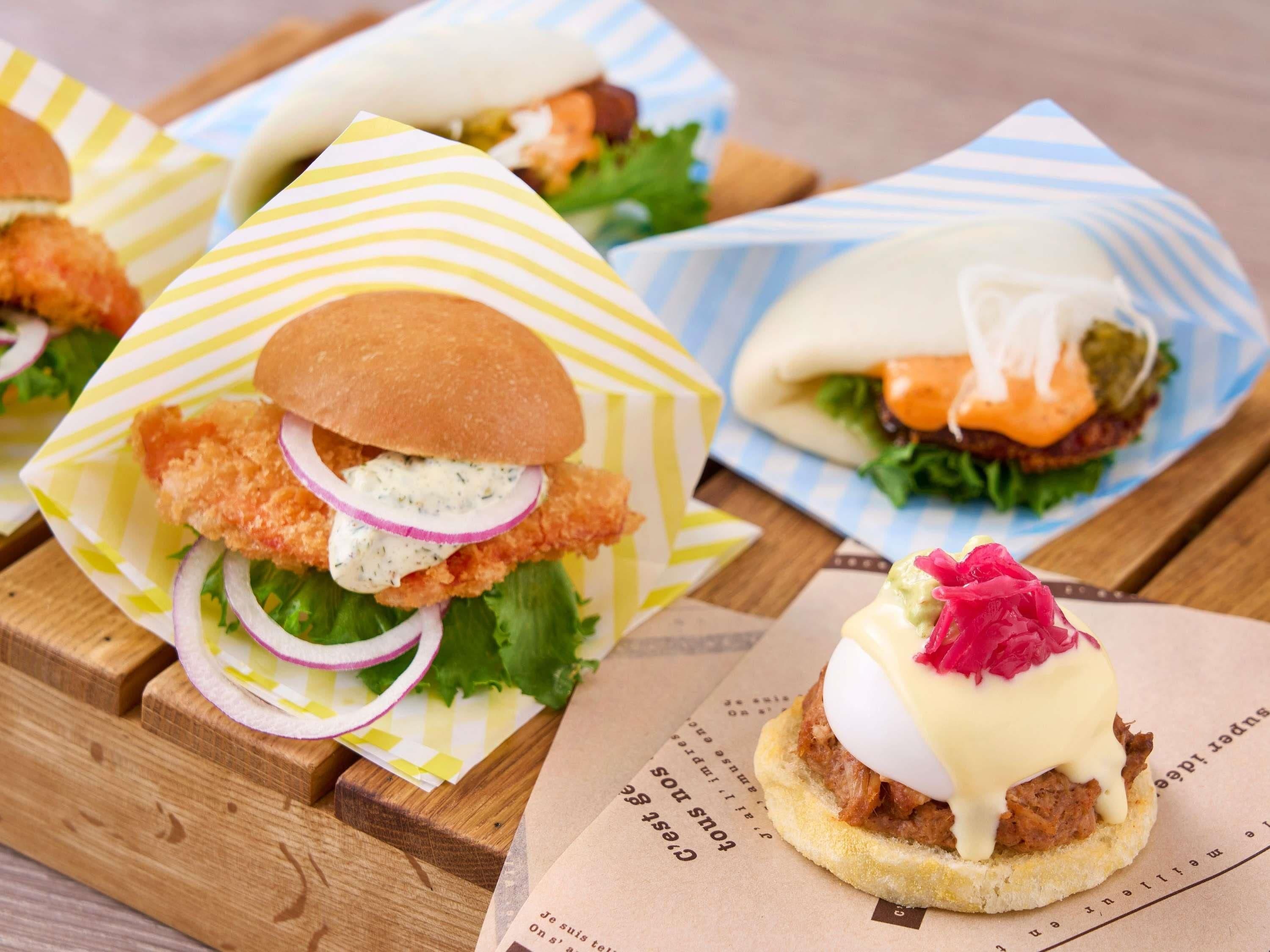 Sandwiches with various toppings and a small dish with a sauce and garnish on a wooden table.