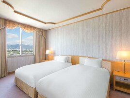 Habitación de hotel con dos camas, un ventanal con cortinas y vista a un paisaje urbano.
