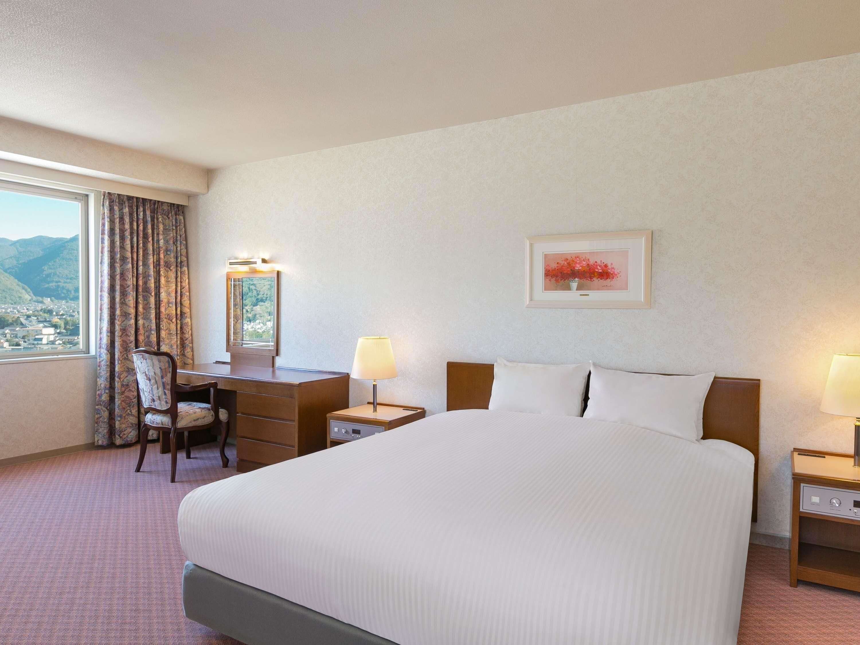 Une chambre d’hôtel avec un grand lit, un bureau avec une chaise, une table de chevet, une lampe et un tableau encadré au mur.