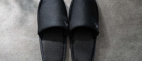 A pair of black slip-on shoes with a textured sole, placed on a textured floor.