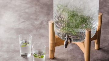 A clear glass container with ice and mint leaves, a metal tap, and two glasses with water and mint leaves.