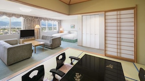 A hotel room with a large window, a bed, a TV, a dining table, and a sliding door.