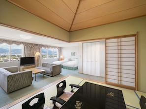 A hotel room with a large window, a bed, a TV, a dining table, and a sliding door.