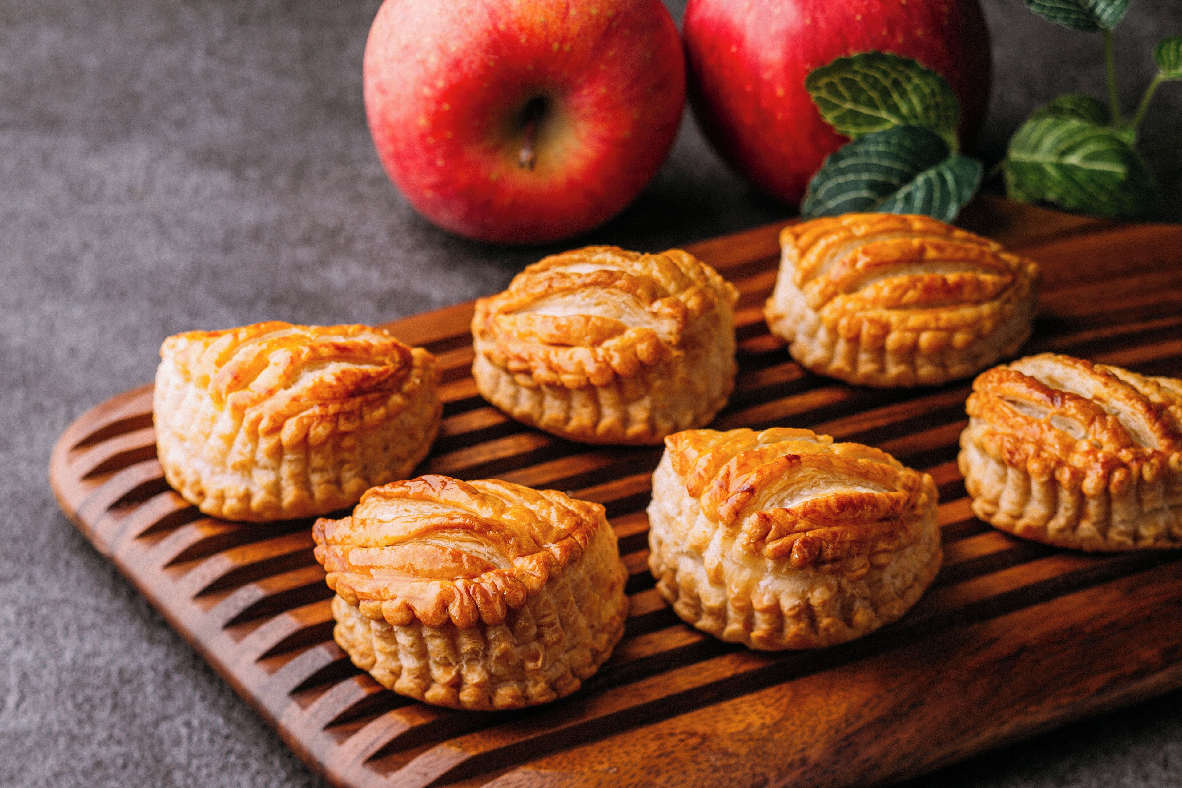 A wooden board with pastries and apples.