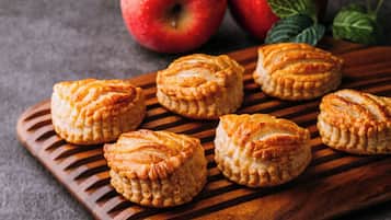 A wooden board with pastries and apples.