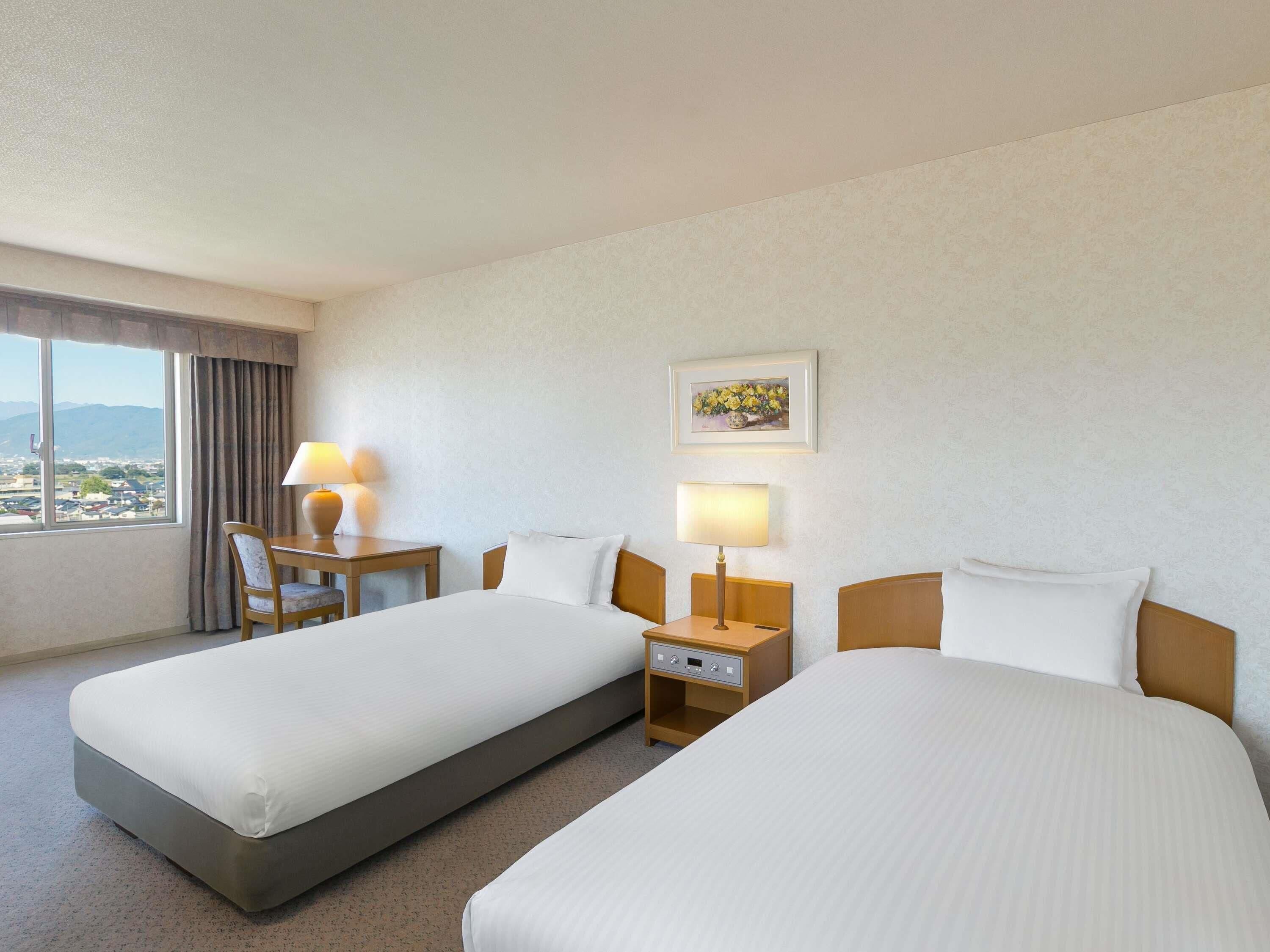A hotel room with two beds, a desk, a chair, and a window with a view.