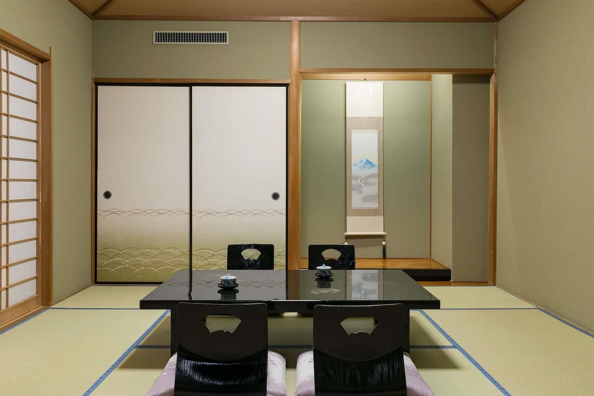 Una habitación japonesa tradicional con suelo de tatami, una mesa baja, dos sillas y puertas correderas.