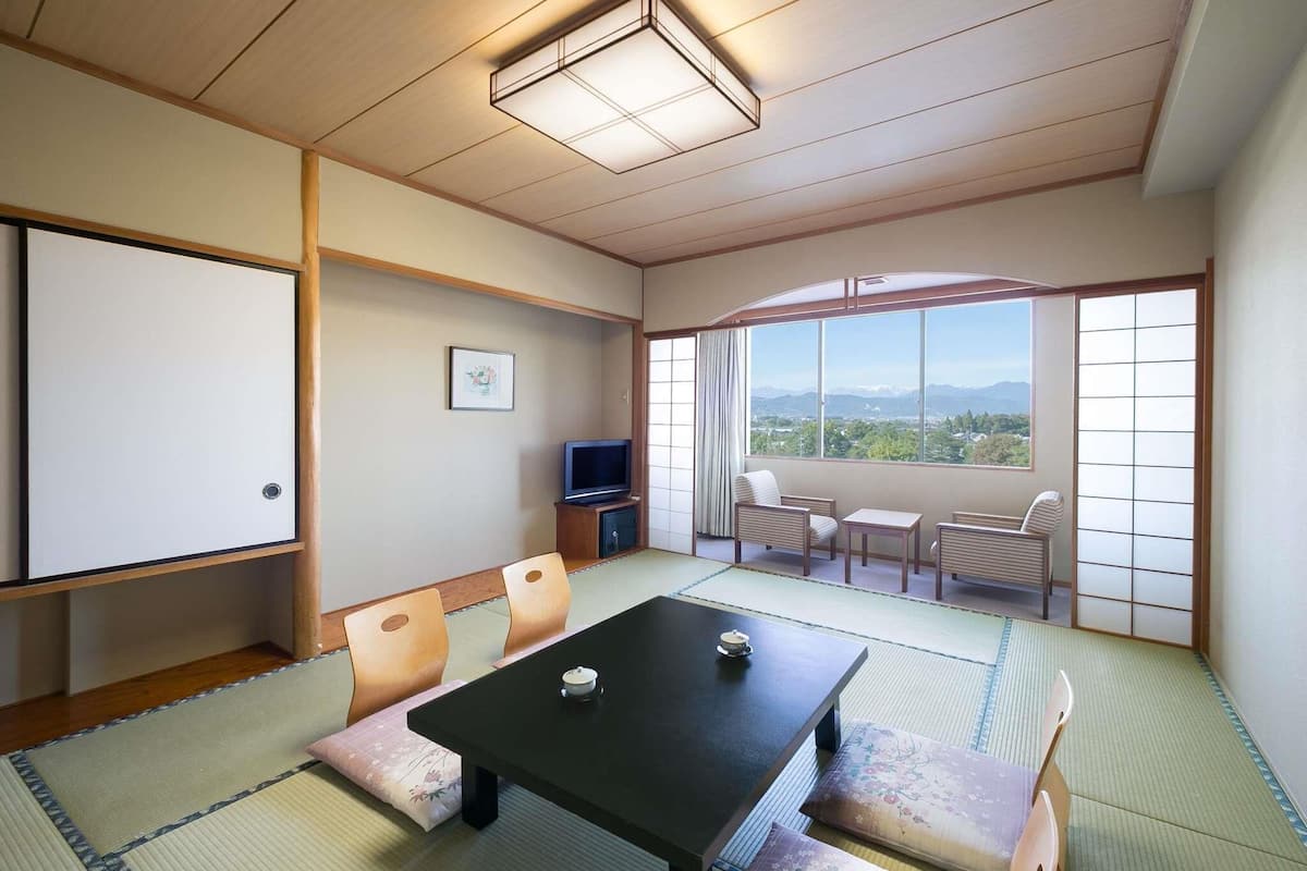 A traditional Japanese room with tatami flooring, a black table, and a view of mountains.