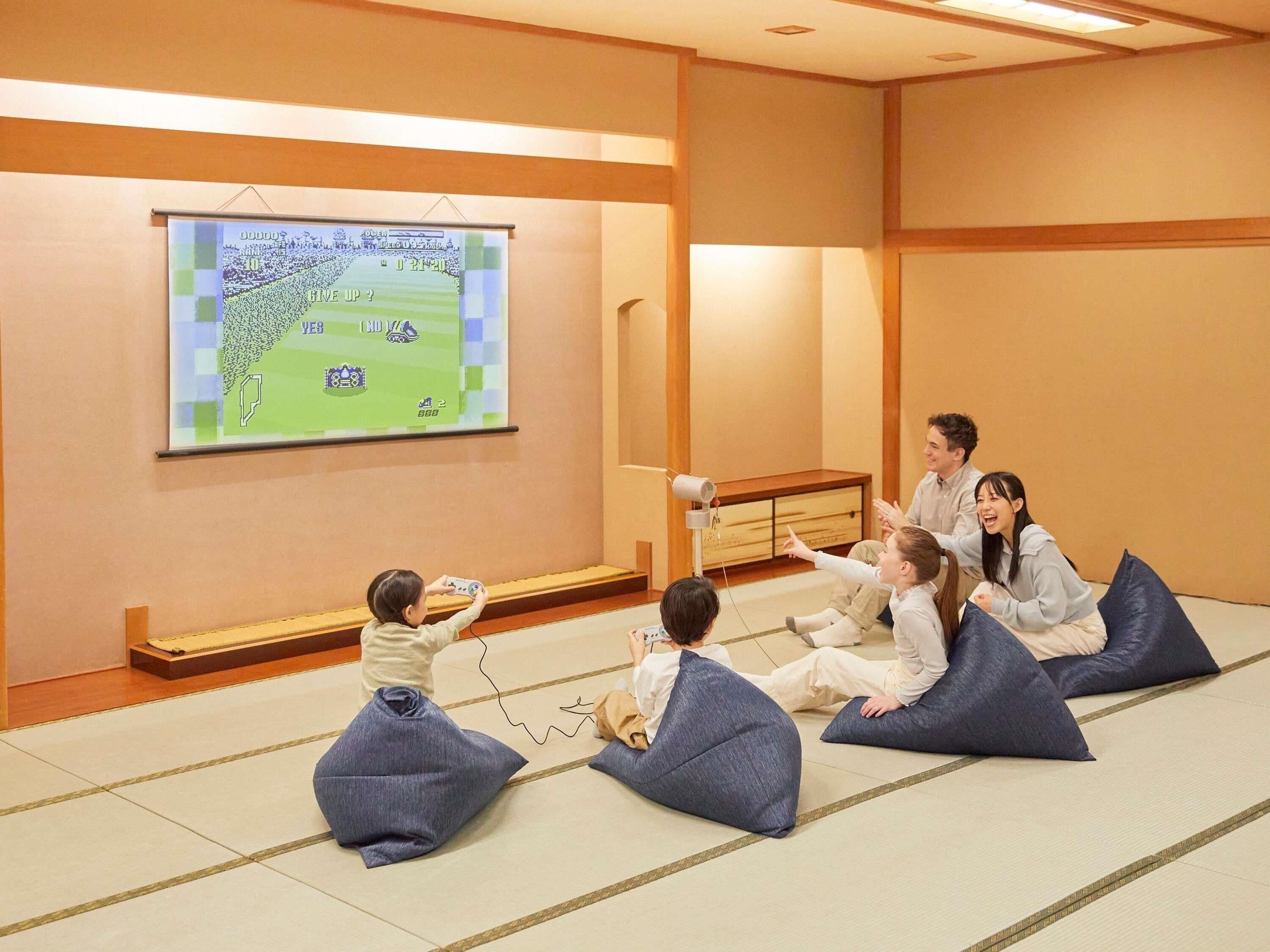 Una habitación con suelo de tatami, una pantalla de proyector mostrando un juego y un divisor de ambiente tradicional japonés.