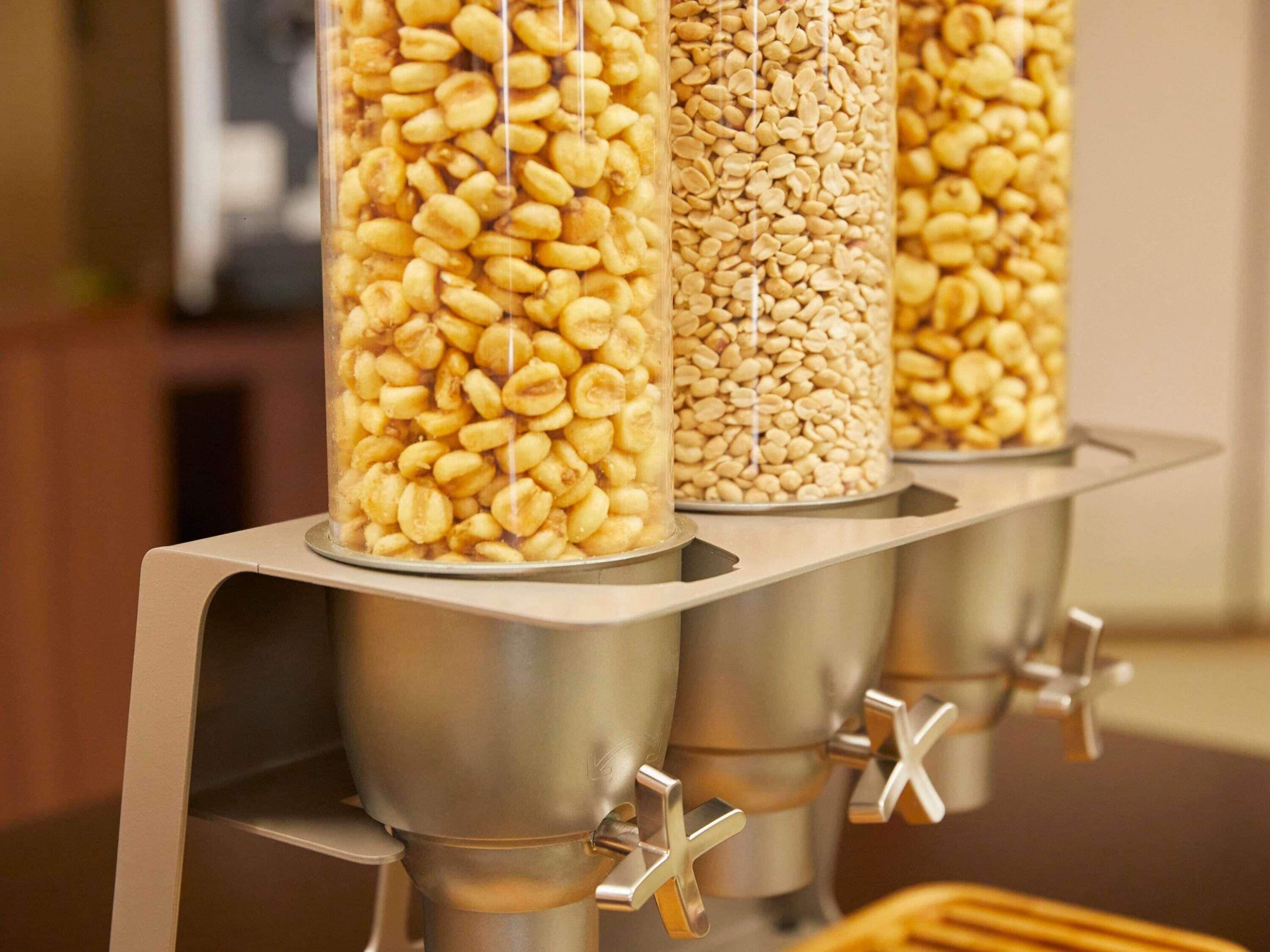 Three transparent containers filled with different types of beans, placed on a metallic stand with levers.