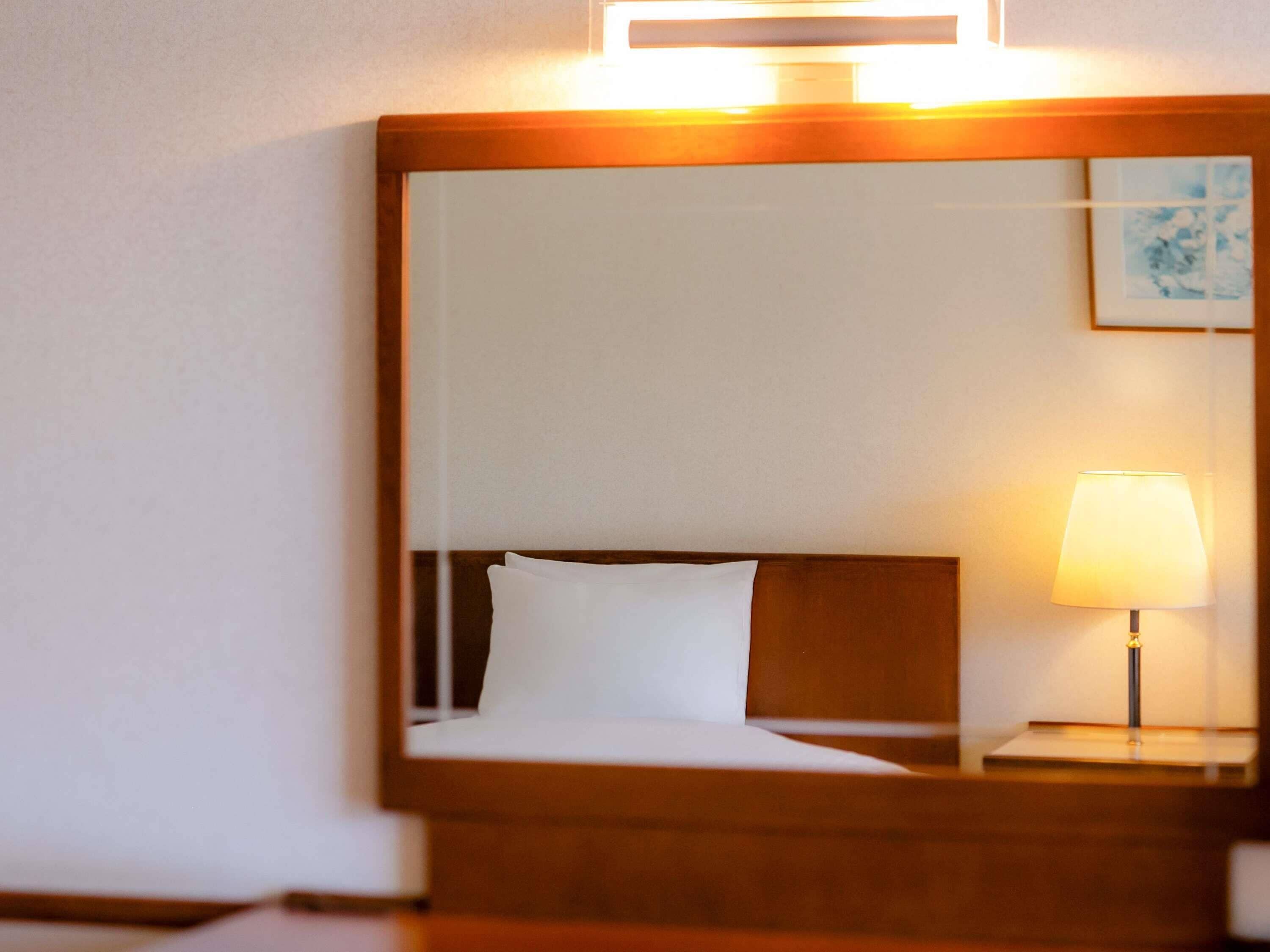Una habitación de hotel con cama, mesita de noche con lámpara y espejo en la pared.