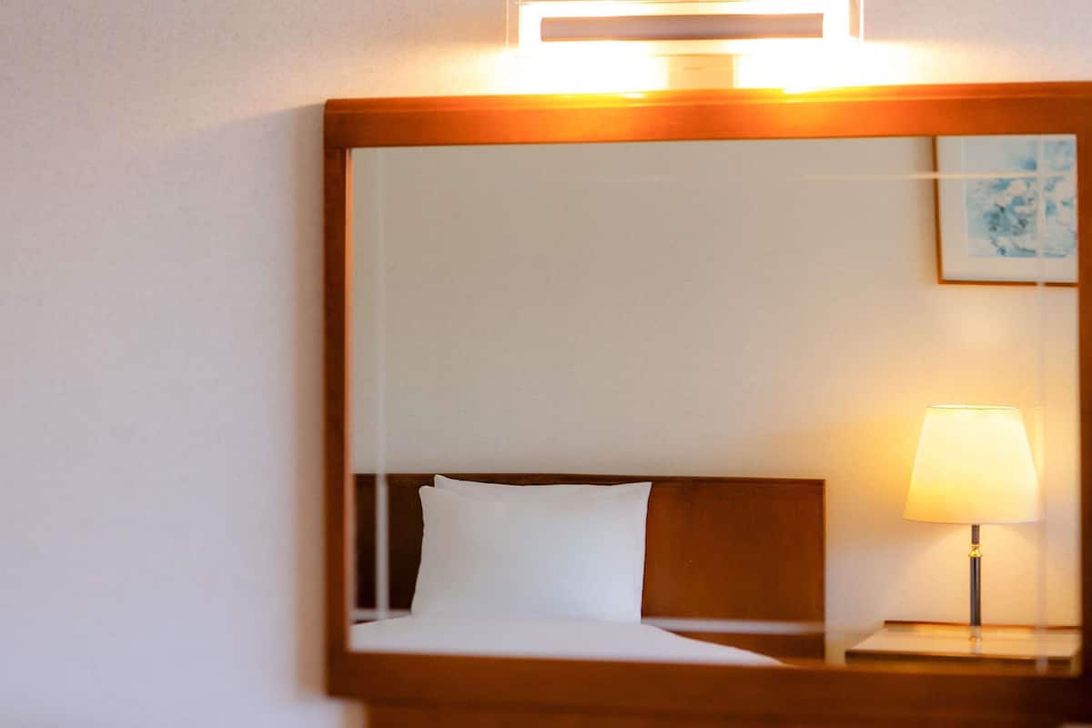 Una habitación de hotel con cama, mesita de noche con lámpara y espejo en la pared.