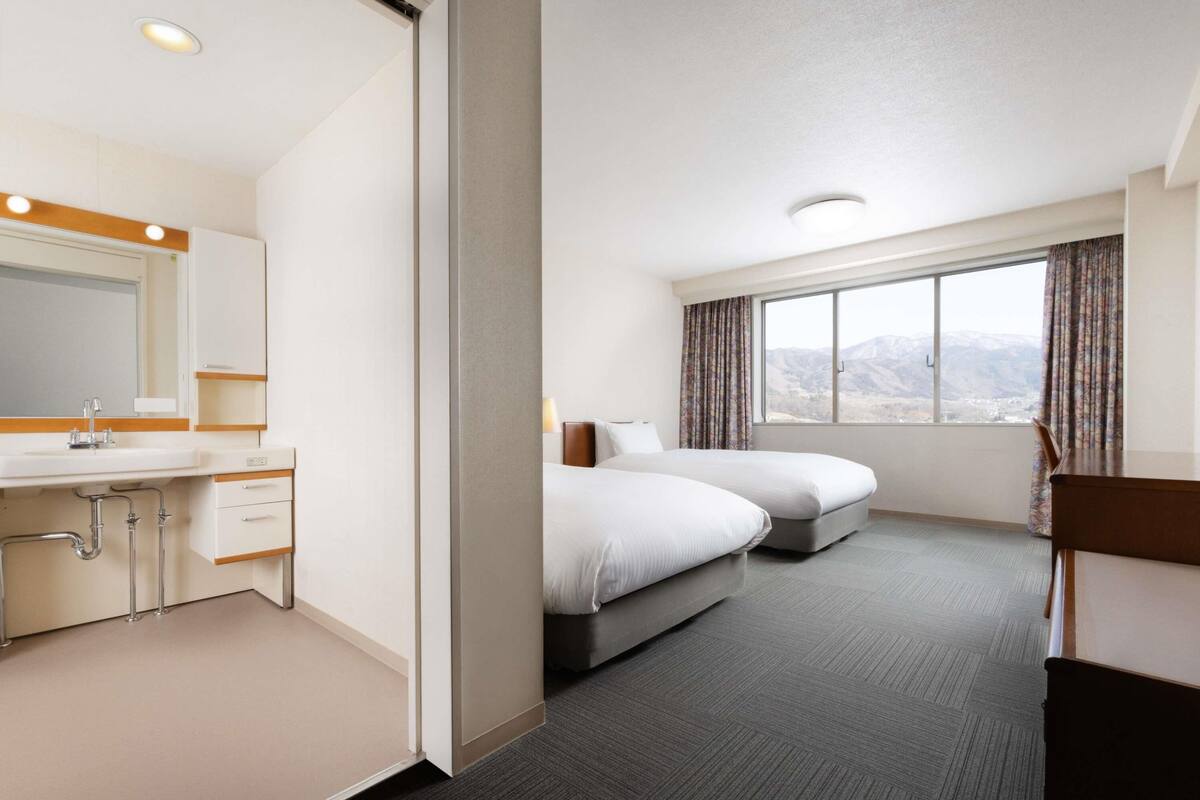 A hotel room with a bed, a desk, a mirror, and a window with a view.