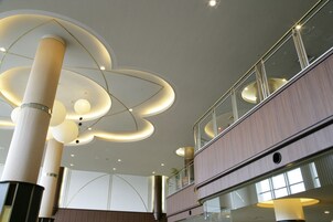 Un interior moderno con techo alto, grandes lámparas cilíndricas y una estructura de varios niveles con barandillas de vidrio.