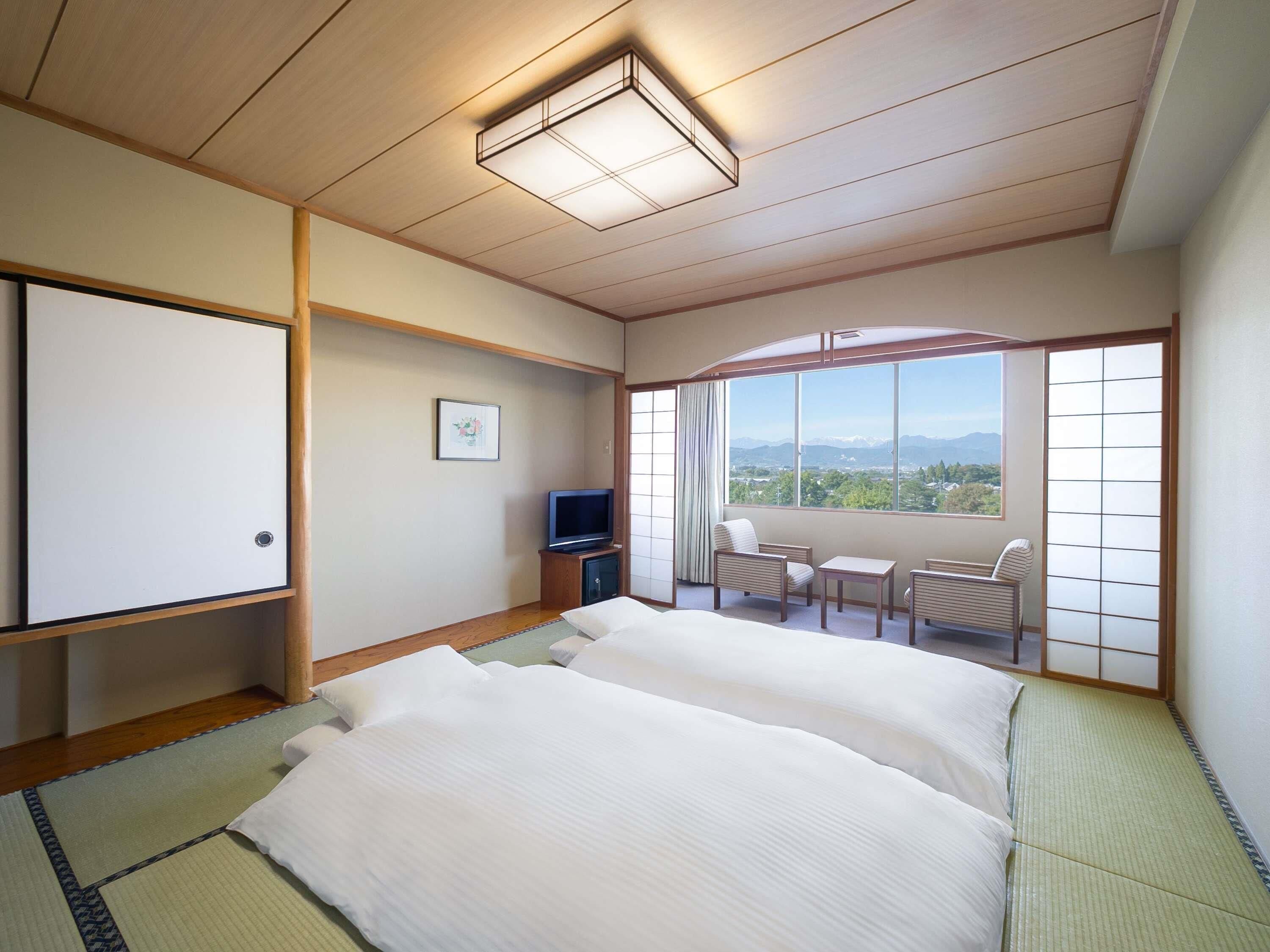 Habitación de hotel con esteras de tatami, una cama, televisión, escritorio y vista a las montañas.