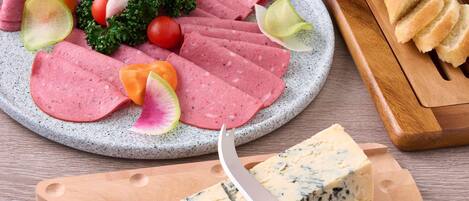Un plato con fiambre, queso y verduras sobre un plato moteado, junto a un cuchillo y una tabla de cortar de madera con queso.