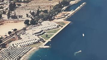 Vue aérienne d’une station balnéaire avec des rangées de villas au bord de la plage, une plage de sable et un port de plaisance.