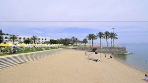 Une plage bordée d’une rangée de bâtiments blancs, de palmiers et de parasols jaunes.