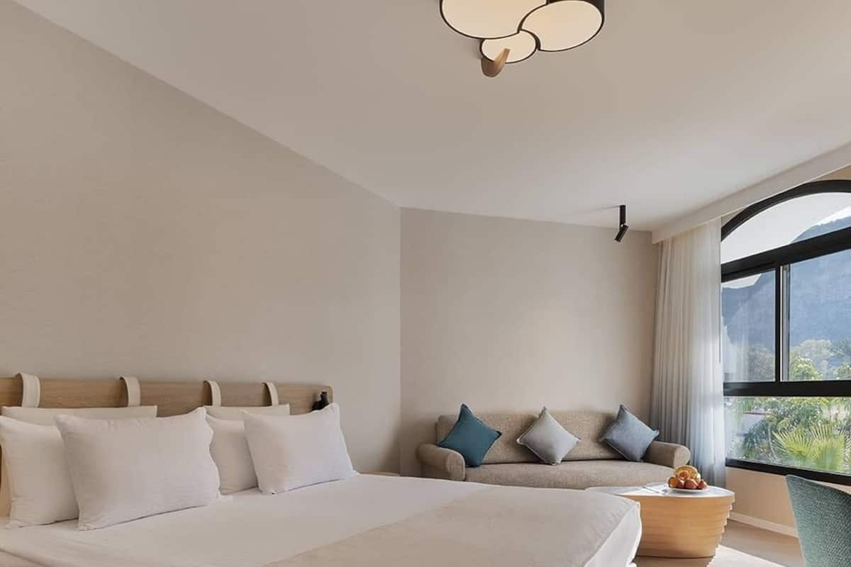 Une chambre moderne avec un grand lit, un canapé et une vue sur la verdure grâce à une grande fenêtre.