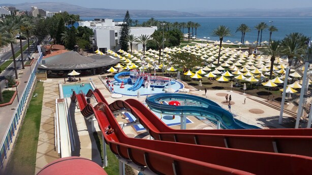 Un parc aquatique doté de nombreux toboggans et d’un espace piscine, le tout entouré de palmiers et de parasols de plage.