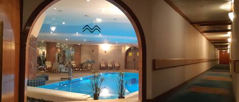 Corredor de hotel com vista para uma piscina, espreguiçadeiras e teto com design de ondas.