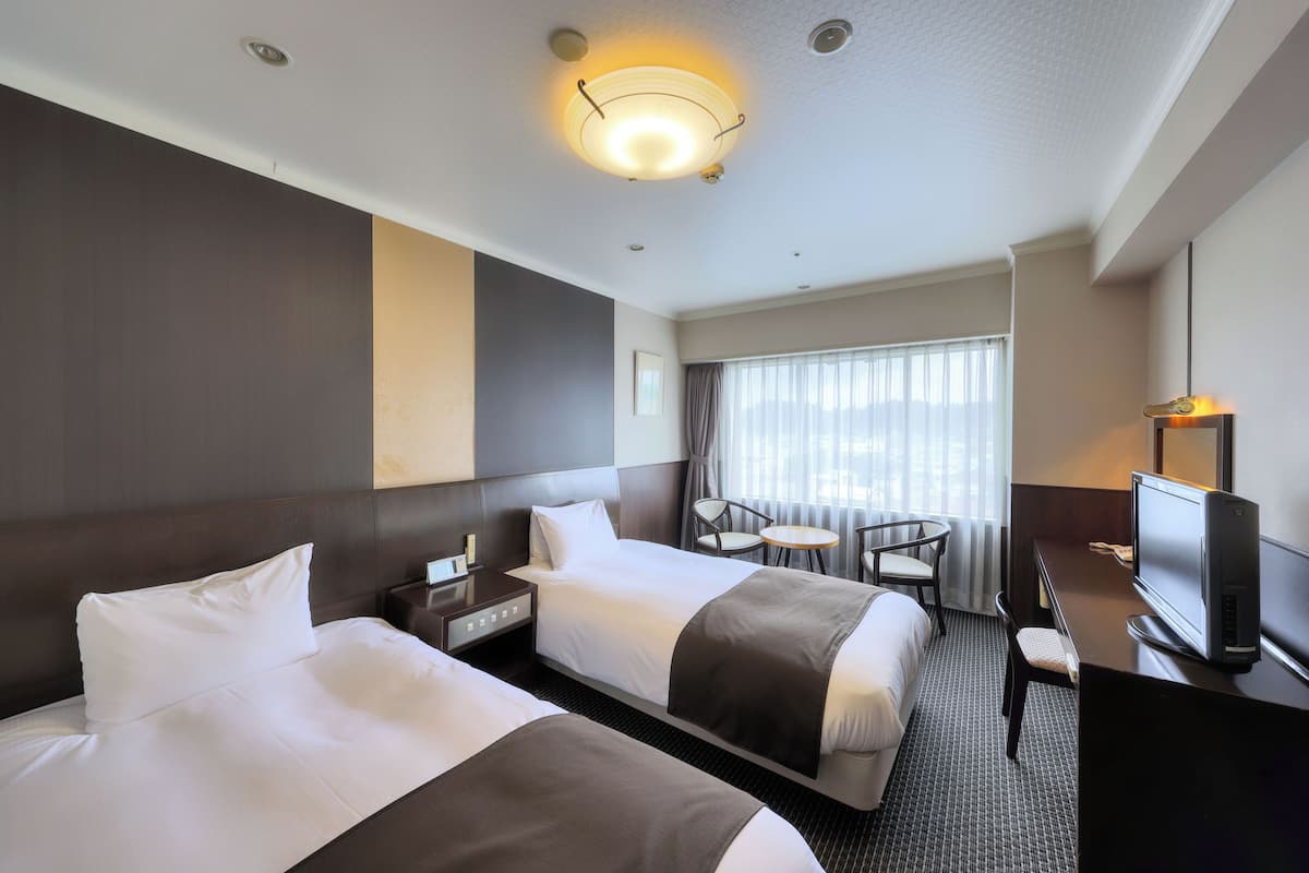 Una habitación de hotel con dos camas, un escritorio con computadora, una silla y televisor.