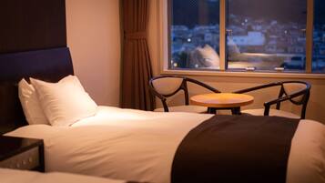 A hotel room with a bed, a small round table, and a window with a view of a town.